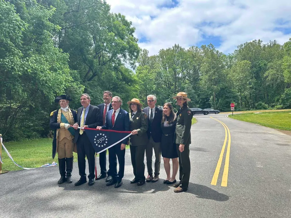 Officials hold an America 250 pennant with the newly rehabilitated GW Parkway in the background (staff photo by Angela Woolsey)