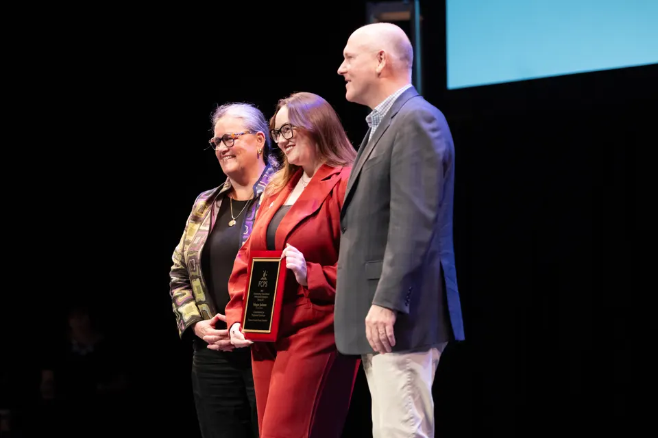 A woman holds an award, stands between two other adults