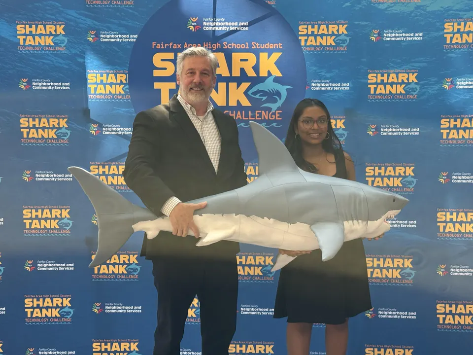 Student and mentor pose with a shark prop at the Fairfax Area High School Student Shark Tank Challenge.