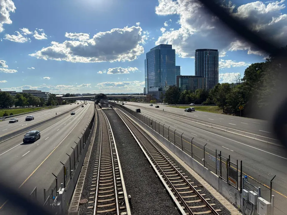 Train tracks leading to the Reston Town Center Metro station flanked by the Dulles Toll Road, seen through a fence (photo by Amy Woolsey)