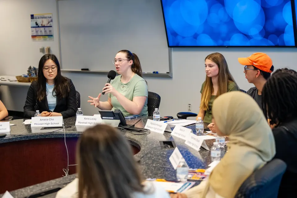 A student holds a microphone as she asks a question.