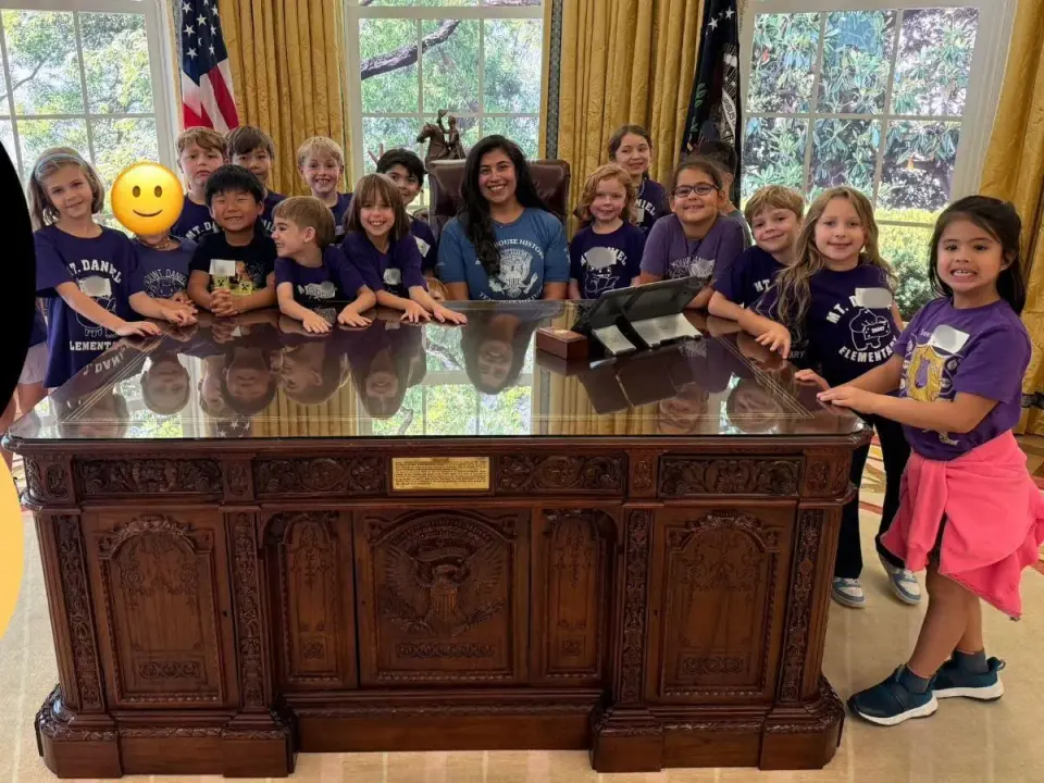 Mount Daniel Elementary School second-grade teacher Gail Bodner with her students at the People's House: White House Experience behind a reproduction of the Resolute Desk....