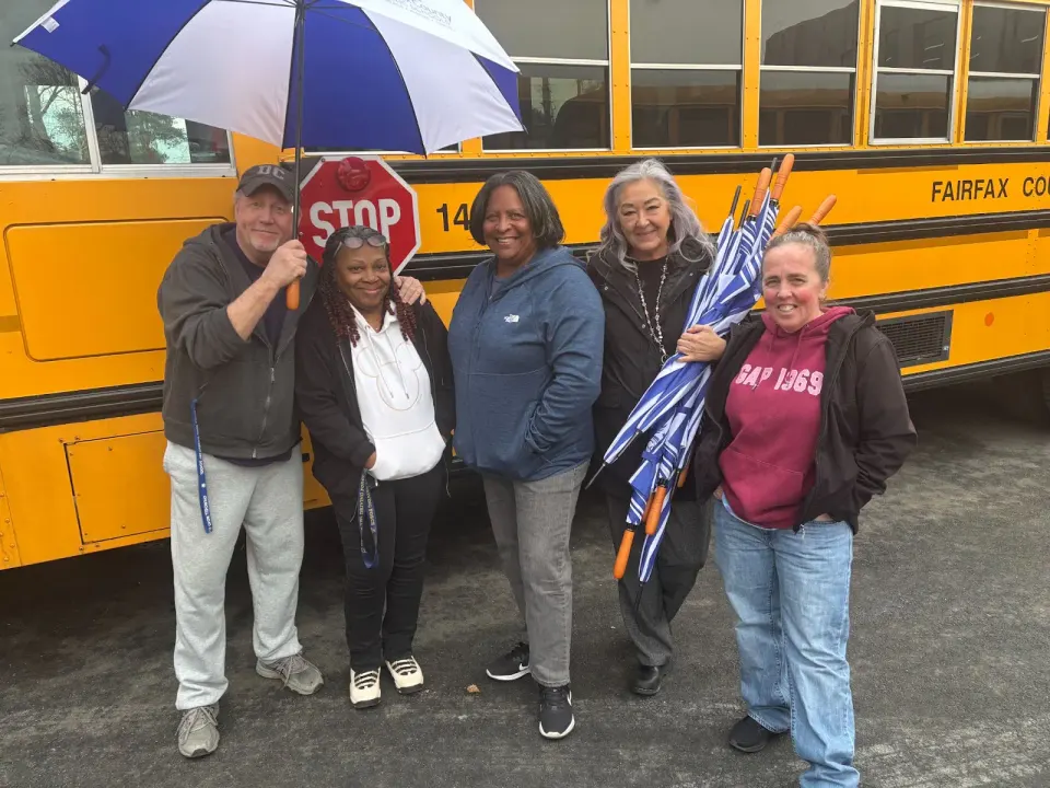 Group of bus drivers in front of a bus receiving umbrellas as a thank you.