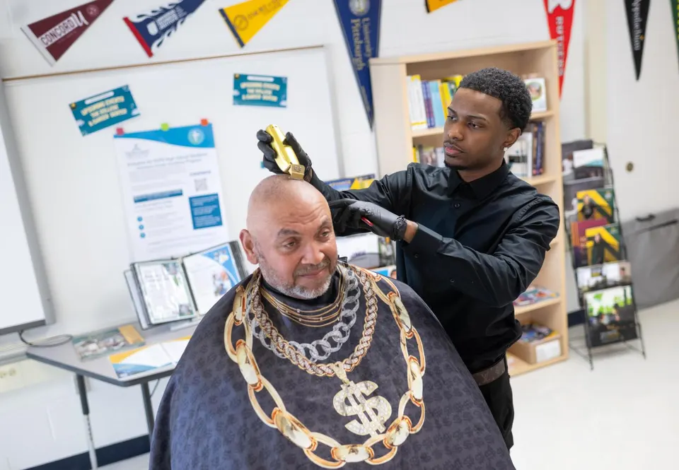 Trey uses electric clippers to shave a teacher's head in a classroom.