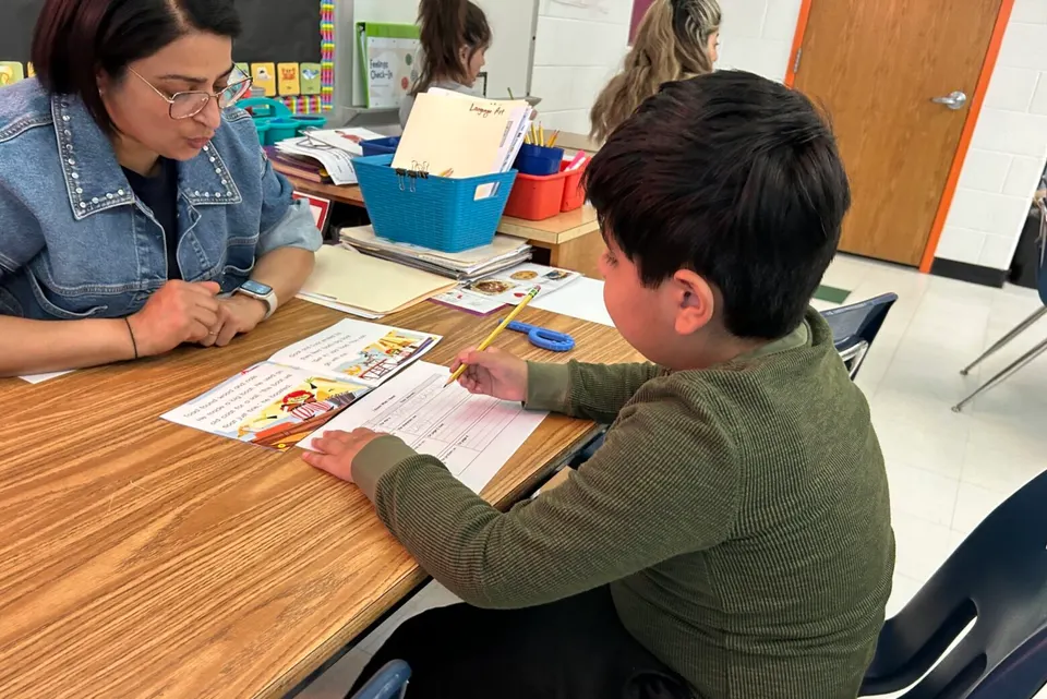 Student works at table with his teacher Nuril Kingsley across