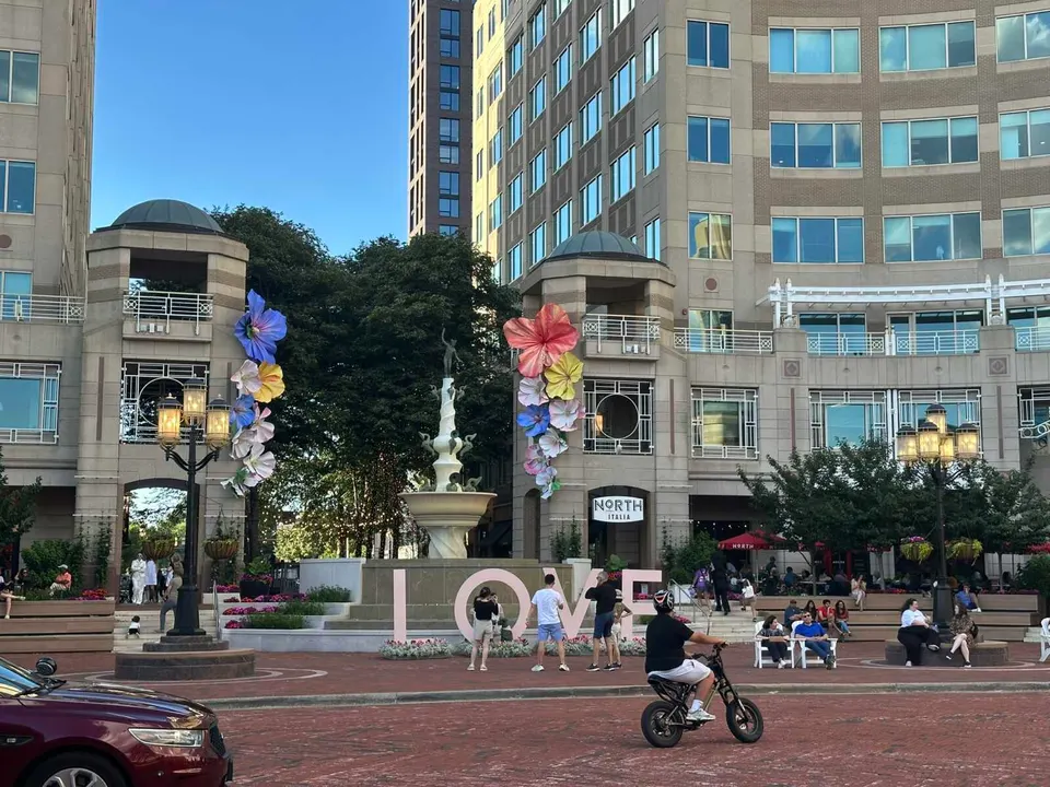 A kid rides a dirt bike, and people take photos of the LOVE sign at Fountain Plaza in Reston Town Center (staff photo by Angela Woolsey)