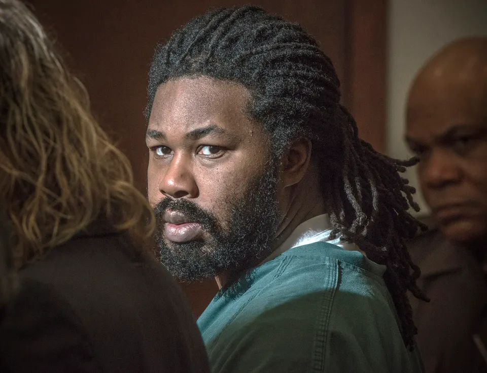 defendant in court in prison jumpsuit looks over left shoulder