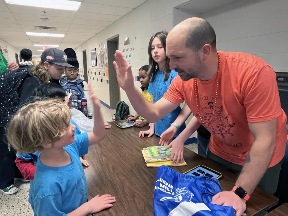 School-Based Technology Specialist Brian Lachance (right) celebrates a student's book donation for the Blue Team.