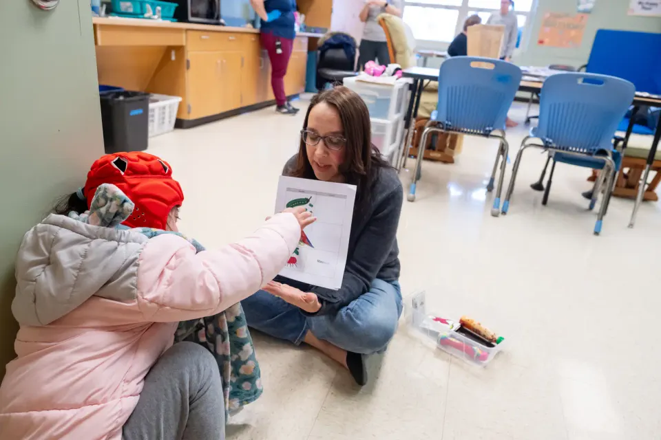 A teacher sits on the floor to work with a student