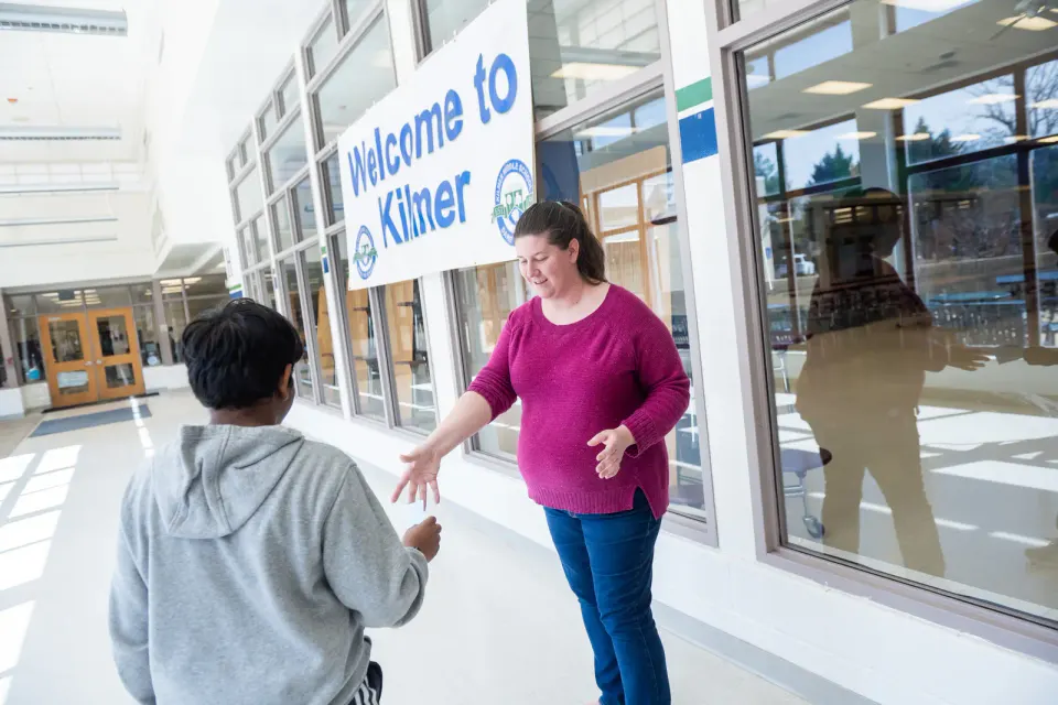 A smiling teacher hands a note to a student. The student looks at the note.