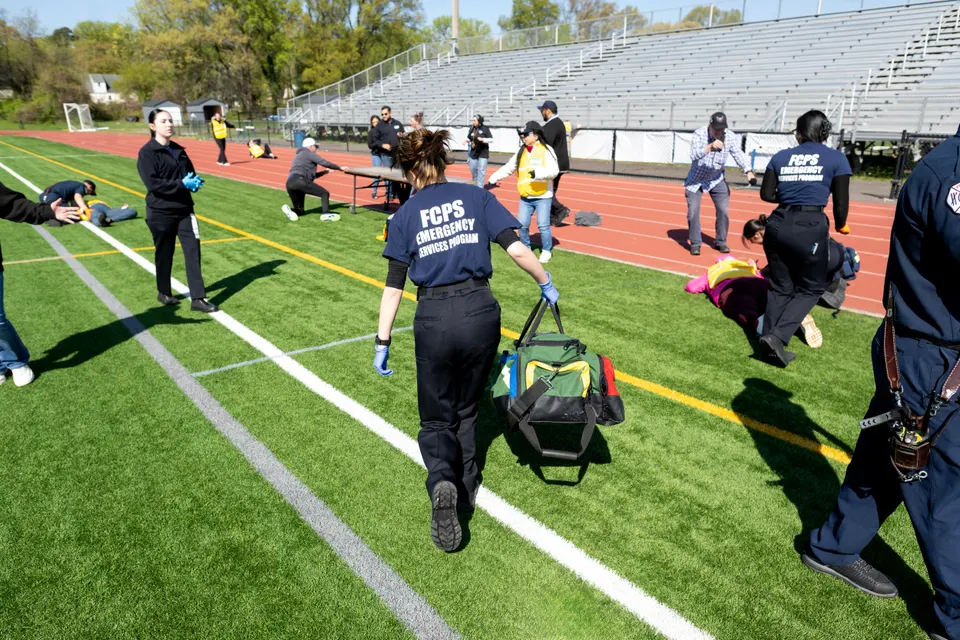 An EMT student carries a bag of medical supplies into a mock emergency scene on a running track.