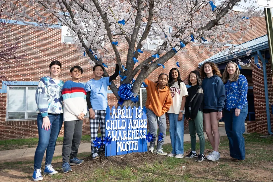 students and staff smile around their decorated blue ribbon tree