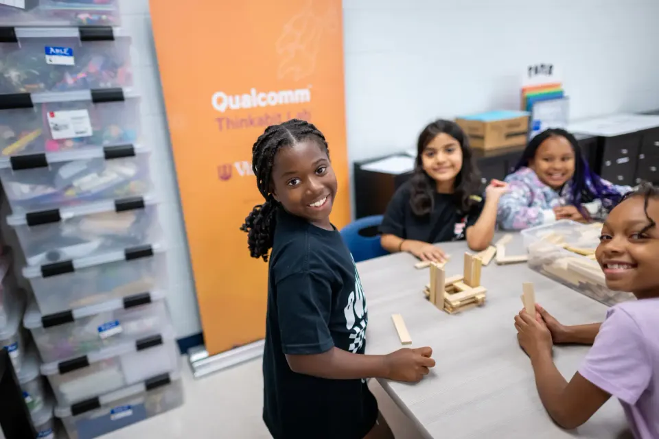 Smiling students sit around a table working together on an engineering project.
