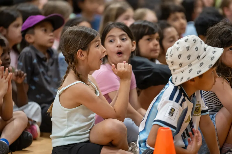 Two young girls sitting with other children look at each other excitedly.