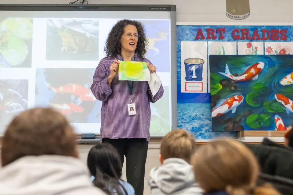 Artist in Residence Penny Hauffe holds up a dyed drawing of a lily pad as she speaks to students.