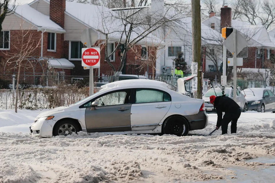 man shovels snow near car that's snowed-in