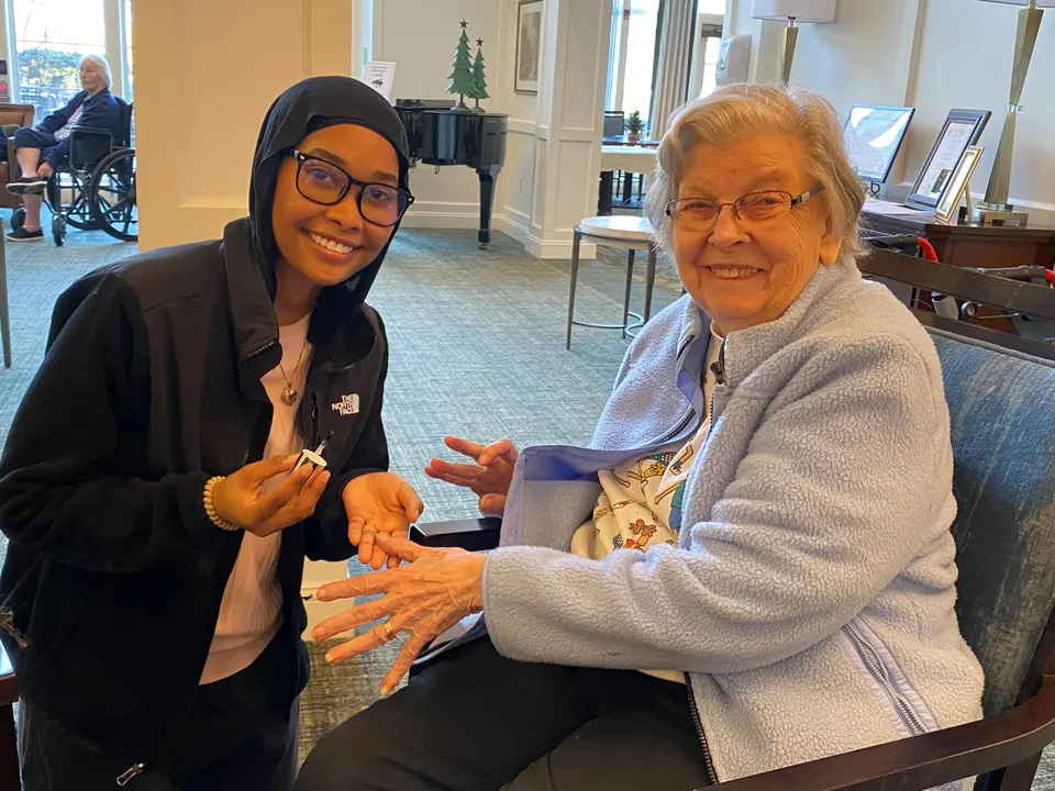 A student sits with a smiling lady as she paints her nails.
