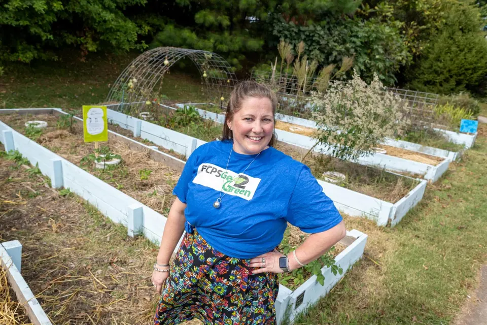A teacher poses in front of raised garden beds.