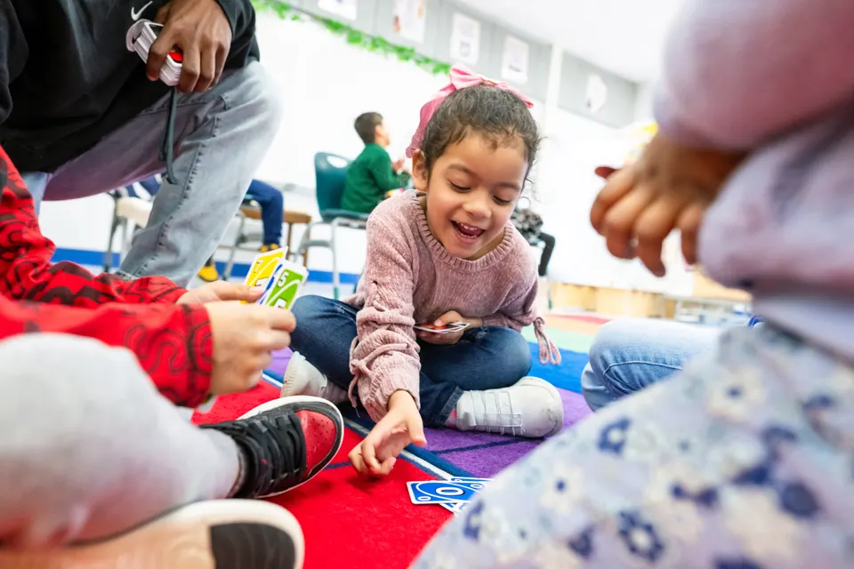 A smiling kindergarten student grabs an UNO! card.