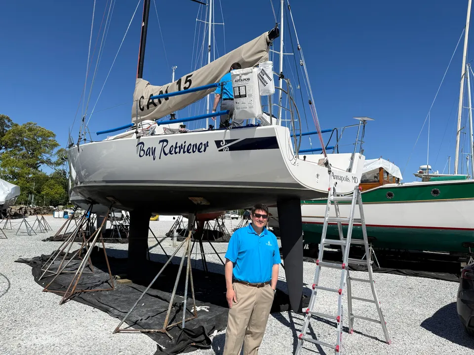 a man in a blue polo stands beneath a large sailboat
