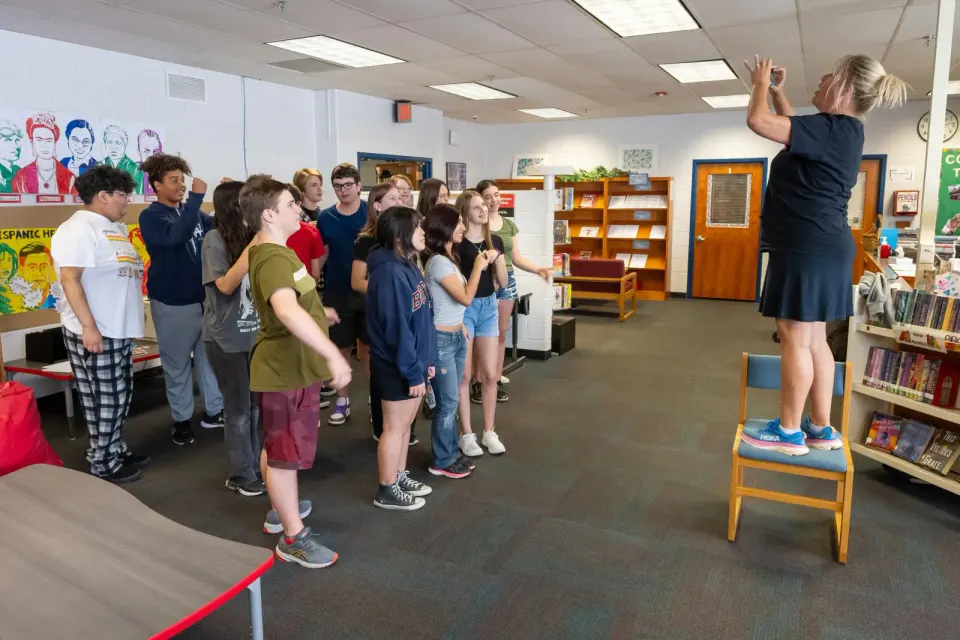 A teacher on a chair takes a selfie of a group of students